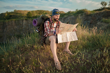 Image showing Young caucasian man with backpack sitting on the top of hill