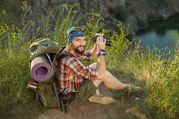 Image showing Young caucasian man with backpack sitting on the top of hill