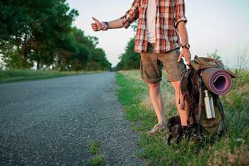 Image showing Young smilimg caucasian tourist hitchhiking along a road.