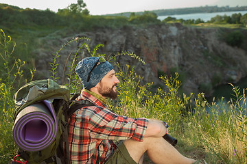 Image showing Young caucasian man with backpack sitting on the top of hill