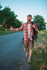 Image showing Young smilimg caucasian tourist hitchhiking along a road.