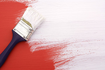 Image showing Paintbrush with white paint painting over red