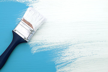 Image showing Paintbrush with white paint painting over blue