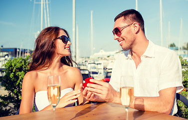 Image showing smiling couple with champagne and gift at cafe