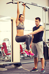 Image showing young woman with trainer doing leg raises in gym