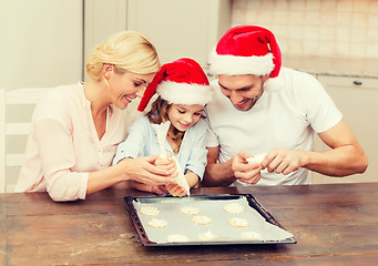 Image showing happy family in santa helper hats making cookies