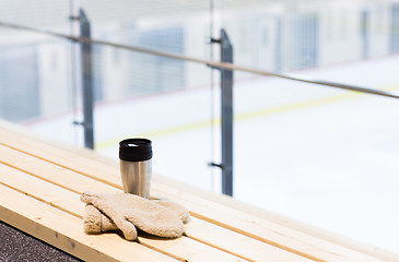 Image showing thermos cup and mittens on bench at ice rink arena