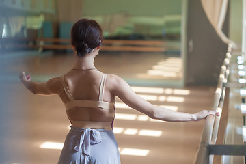 Image showing classic ballet dancer posing at barre on rehearsal room background