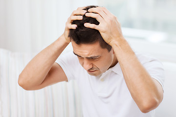 Image showing unhappy man suffering from head ache at home