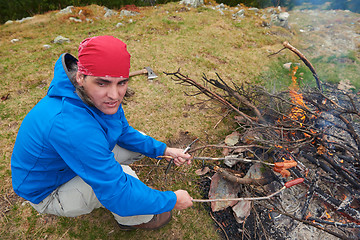 Image showing hiking man prepare tasty sausages on campfire