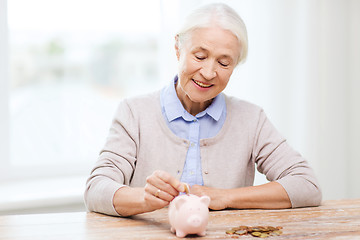 Image showing senior woman putting money to piggy bank at home