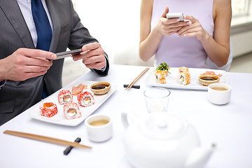 Image showing close up of couple with smartphones at restaurant