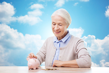 Image showing senior woman putting money to piggy bank