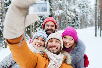 Image showing smiling friends with camera in winter forest