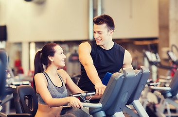 Image showing happy woman with trainer on exercise bike in gym