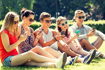 Image showing smiling friends with smartphones sitting on grass