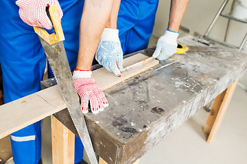 Image showing close up of builders with arm saw sawing board