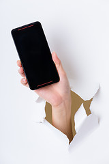 Image showing Hand holding mobile phone bursting through paper