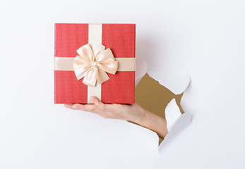 Image showing Woman hand hold with present box break through the paper wall