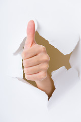 Image showing Thumb up hand gesture through a hole in paper