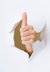 Image showing Hand with thumb up through a hole in paper