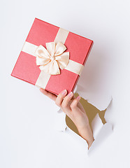 Image showing Hand hold with giftbox break through the paper wall