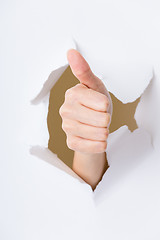 Image showing Hand with thumb up through a hole in paper