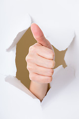 Image showing Hand with thumb up through a hole in paper