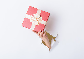 Image showing Hand holding pink gift box through the paper hole 