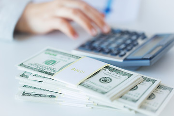 Image showing close up of hand counting money with calculator