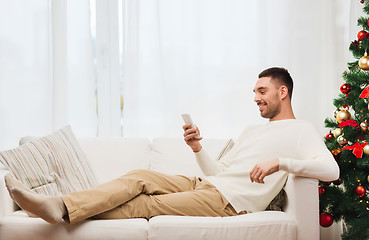 Image showing smiling man with smartphone at home for christmas