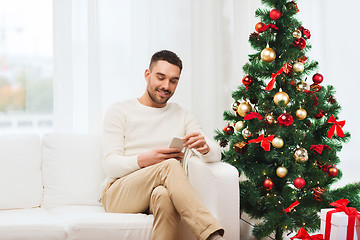 Image showing smiling man with smartphone at home for christmas