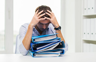 Image showing sad businessman with stack of folders at office