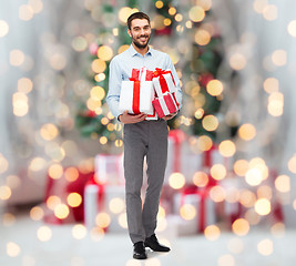 Image showing happy man holding gift boxes over christmas lights