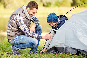 Image showing happy father and son setting up tent outdoors