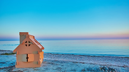 Image showing Toy house made of corrugated cardboard in the sea coast at sunset.