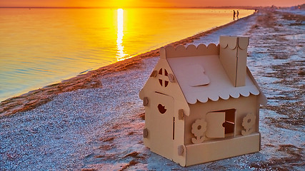 Image showing Toy house made of corrugated cardboard in the sea coast at sunset.