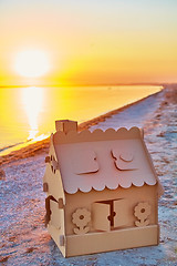 Image showing Toy house made of corrugated cardboard in the sea coast at sunset.