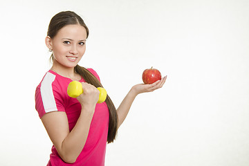 Image showing Sportswoman holding a dumbbell in your right hand and an apple in his left hand