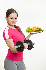 Image showing Sportswoman holding a dumbbell and a bowl of fruit