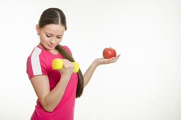 Image showing Athlete shakes muscles of his right hand holding an apple and a dumbbell in your left hand