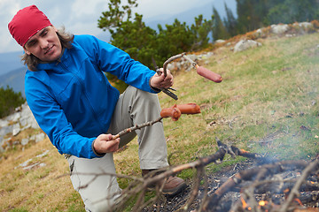 Image showing hiking man prepare tasty sausages on campfire