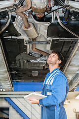 Image showing Mechanic With Clipboard Examining Under Car In Garage