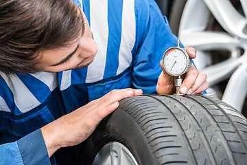 Image showing Mechanic Pressing Gauge Into Tire In Garage