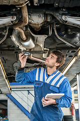 Image showing Mechanic Examining Exhaust System Of Car With Flashlight