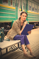 Image showing beautiful middle-aged woman-traveler sitting on a bench, holding