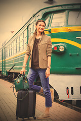 Image showing smiling middle-aged woman with luggage near old train