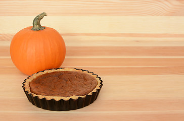 Image showing Mini pumpkin pie with orange pumpkin on wood