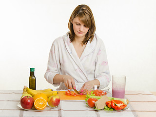 Image showing Happy housewife sitting at the table and cut the tomato salad