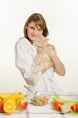 Image showing Young girl sitting at the table with vegetarian dishes and holds a disgruntled cat